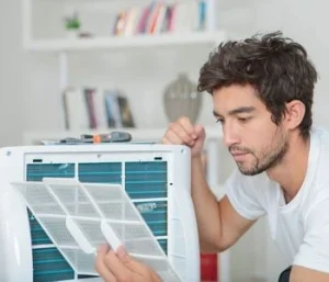 "A man inspecting the filter of an air conditioner, performing maintenance and cleaning to ensure optimal performance. Regular air conditioning service helps improve efficiency, prolong lifespan, and maintain indoor air quality."