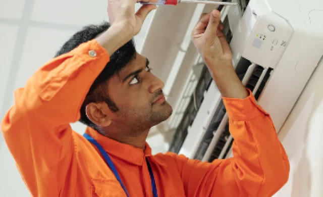 "Indian technician setting up an air conditioning unit with a screwdriver, demonstrating professional HVAC installation services."